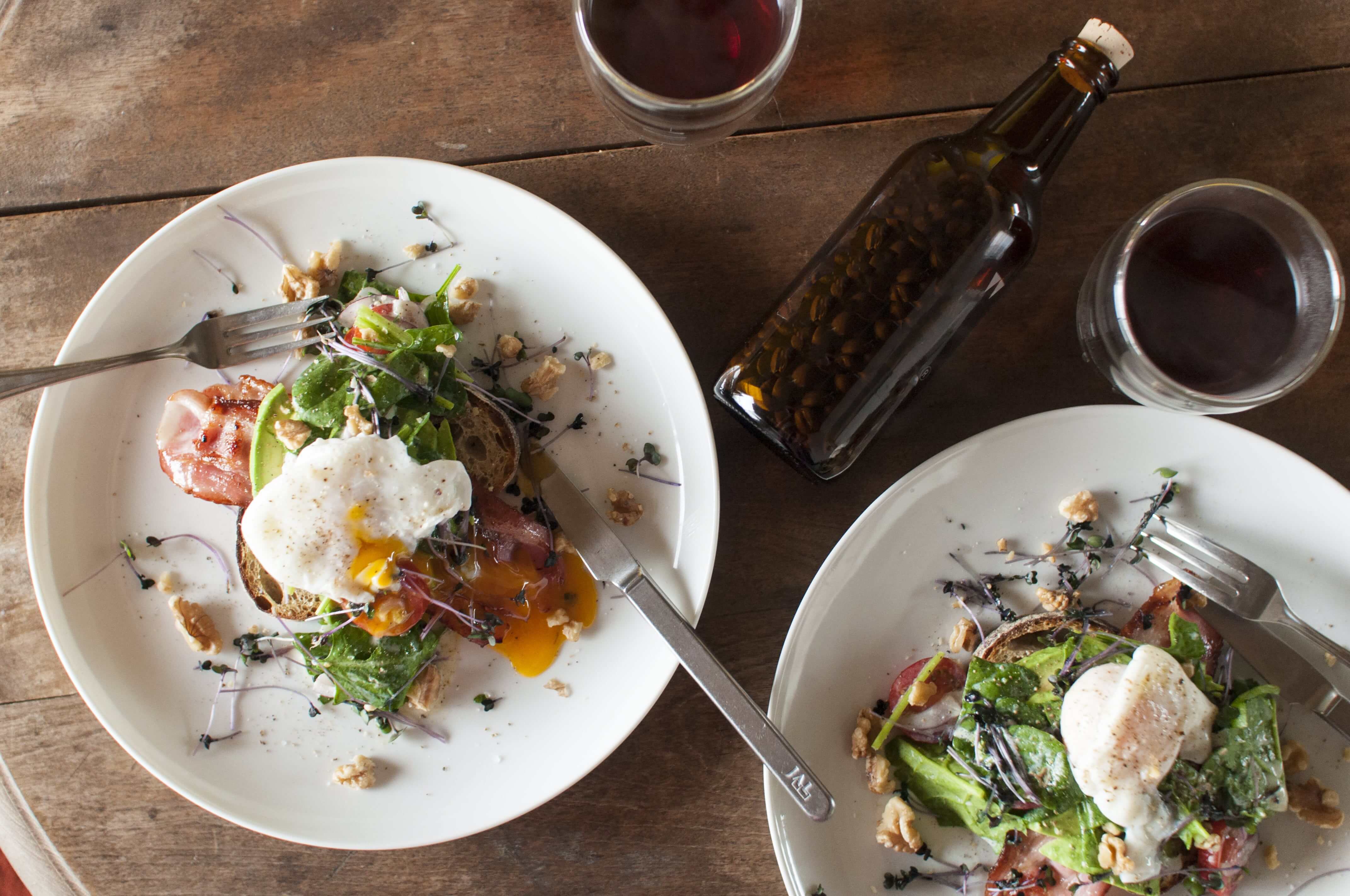 top view of perfect Sunday brunch. Australian style open sandwich with vegetables, avocado, poached egg, bacon and coffee on wooden table